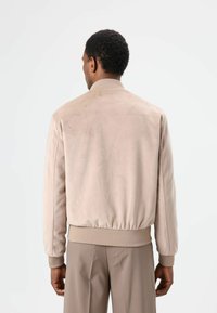 Lichtbeige suède bomberjack met geribde boorden aan de mouwen en zoom, met een gladde afwerking en een ontspannen pasvorm. De achteraanzicht toont een eenvoudig ontwerp.