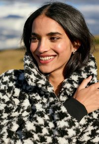 Jachetă din fleece cu un model houndstooth alb-negru, având un guler înalt, închidere cu fermoar și manșete ribbate. Material moale, texturat.