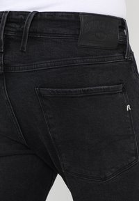 Svarta denimbyxor med texturerad yta, bakficka och en märkespatch av läder i midjan.