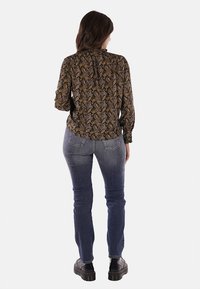Blusa nera a maniche lunghe con motivo paisley, infilata in jeans blu aderenti, con scollatura tonda e dettaglio arricciato sul retro. Stivali neri visibili.