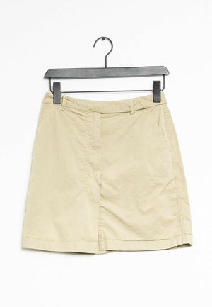 Falda de algodón beige con un diseño recto, presenta una abertura frontal, bolsillos laterales y una textura suave. Cuelga de una percha negra.