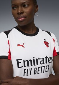 Hvid fodboldtrøje med røde og sorte accenter, med et Puma-logo og teksten "Emirates FLY BETTER". Korte ærmer og rund halsudskæring.
