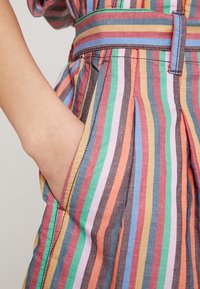 Tissu rayé multicolore avec un design plissé ; doté d'une ceinture et de poches latérales. Matière texturée et légère.