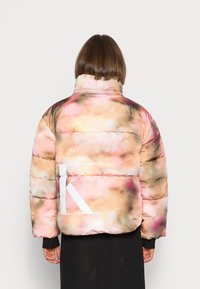 Giacca imbottita con un motivo floreale in tonalità di rosa pallido e beige, colletto alto e grande logo bianco sul retro.