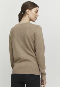 Beige sweater with a rounded neckline and long sleeves, featuring ribbed cuffs and hem. Smooth texture, fitted design, and minimal detailing.