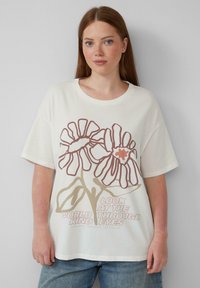 Crème oversized t-shirt met kleurrijk bloemig graphic design in bruin en perziktonen, met de tekst "Kijk naar de wereld door vriendelijke ogen."