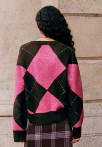 Schwarzer und pinker Strickpullover mit Diamantmuster, mit geripptem Halsausschnitt und Bündchen; weiche Textur, lockere Passform und überschnittene Schultern.