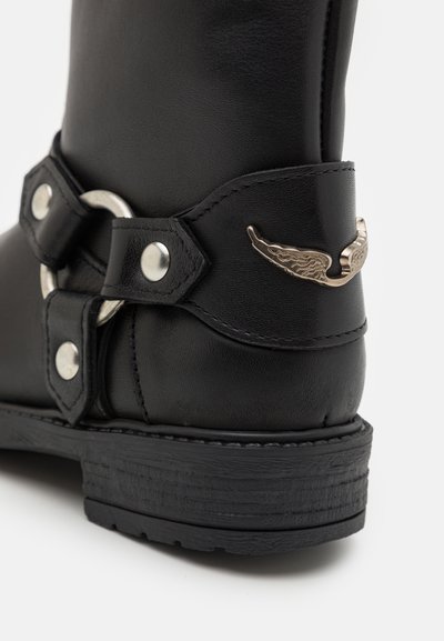 Mustat nahkaiset nilkkurit, joissa on hopeinen siipikoriste, metallinen solki ja teksturoitu pohja. Sileä pinta, jossa on koristeellista ompelua.