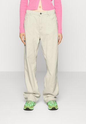 Person wearing loose beige corduroy pants, pink cropped ribbed sweater, and neon green sneakers, standing against a plain background.