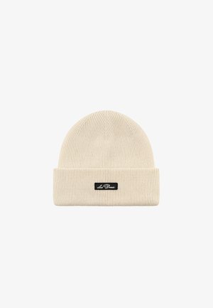 Cream-colored beanie hat with ribbed texture, folded cuff, and a black label stitched with "Les Deux."