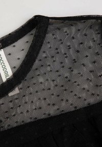 Czarna siateczkowa tkanina z kropkowanym wzorem, z okrągłym dekoltem. Tekstura wydaje się miękka i lekka, idealna do warstwowego ubierania się.