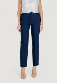 Pantaloni tailored blu navy con vestibilità slim, davanti piatto e dettagli con passanti per cintura, abbinati a un top bianco in stile corsetto con bottoni.