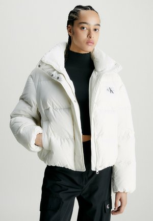 Chaqueta de plumas blanca con un cuello alto, cierre de cremallera y logo de parche. Presenta textura acolchada y mangas grandes y acolchadas.