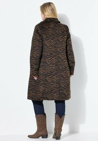 Bruine jas met zebra-patroon, met een kraag, lange mouwen en zijzakken. Gedragen over donkere jeans en bruine cowboylaarzen.