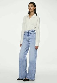 Gaiši izbalināta džinsa bikses ar plašu kāju un augstu jostasvietu, apvienotas ar lielizmēra, gaišas krāsas pogājamu krekls. Mīksta auduma struktūra, brīvs piegriezums.