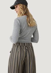 Top de manga larga gris con textura acanalada combinado con pantalones de tiro ancho a rayas en negro y beige, con un ajuste relajado y cinturilla elástica.
