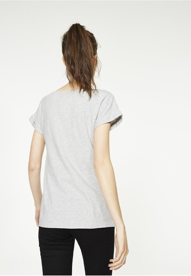 Camiseta de algodón gris con mangas cortas enrolladas, con un corte relajado y un escote redondeado, combinada con pantalones negros.