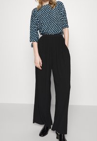 Haut à motifs bleus avec des manches trois-quarts, associé à un pantalon plissé noir taille haute. Tissu lisse avec une coupe décontractée. Bottines noires.