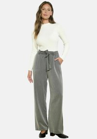 Pilkos, dryžuotos plačios kelnes su diržu ir šoninėmis kišenėmis, derinamos su baltu raštuotu ilgomis rankovėmis marškinėliais. Juodi batai.