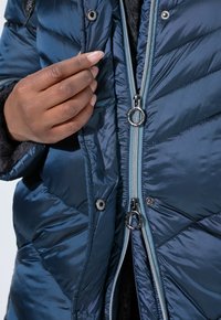 Giubbotto imbottito blu navy con motivo a rombi, zip argentata e chiusure a bottoni a pressione. Fodera interna morbida e testurizzata per l'isolamento.
