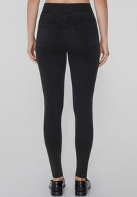 Vaqueros elásticos negros con una cintura alta, dos bolsillos traseros y un diseño ajustado. Textura de tela suave con costuras mínimas.