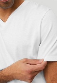 Witte katoenen v-hals t-shirt met korte mouwen. Ronde halslijn en een zachte textuur, met een hand die de mouwzoom aanpast.