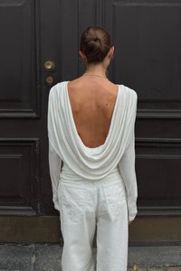 Weißes Langarmoberteil mit offenem, drapiertem Rücken, kombiniert mit weißen, hochtaillierten Hosen. Glattes Material mit lockerer Passform und minimalistischen Design.