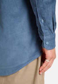Lichtblauw corduroy overhemd met verticale ribbels, knoopsluiting aan de mouwen en een gebogen zoom, gecombineerd met beige stoffen broek.
