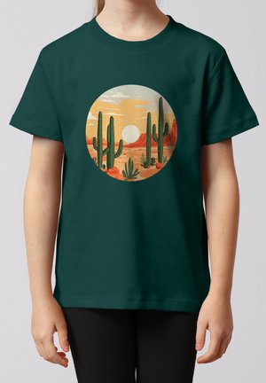 Kind trägt dunkelgrünes T-Shirt mit rundem Wüstenlandschafts-Design, das hohe Kakteen, rote Felsen und untergehende Sonne zeigt.