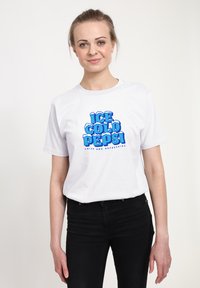 Bílý bavlněný tričko s modrou grafickou potiskem, na kterém je nápis "ICE COLD PEPSI" s akcenty připomínajícími sníh, doplněný o černé džíny.