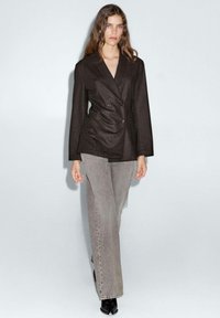 Blazer noir à double boutonnage avec des revers structurés, associé à un jean large gris clair et des bottines noires. Texture de tissu lisse.