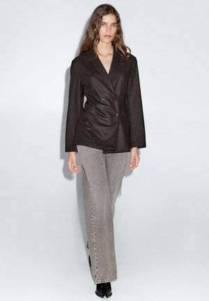 Zwarte dubbelgeknoopte blazer met gestructureerde revers, gecombineerd met lichtgrijze wijde jeans en zwarte enkellaarsjes. Soepel stoffen textuur.