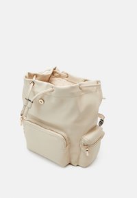 Mochila de cuero beige con acabado texturizado, cierre de cordón, bolsillo frontal con cremallera y detalles en hardware dorado.