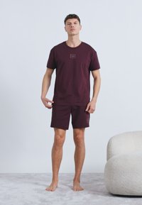 Σετ ανδρικό με μπορντό κοντομάνικη μπλούζα και σορτς από απαλό βαμβάκι, με μίνιμαλ σχεδιασμό και μικρά λογότυπα και στα δύο κομμάτια.