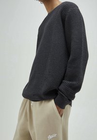 Ciemny, teksturowany sweter z żebrowanym wzorem, okrągłym dekoltem i długimi rękawami. Połączony z jasnobeżowymi joggerami z przeszyciami.