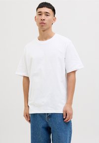 Weißes Baumwoll-T-Shirt mit Rundhalsausschnitt und kurzen Ärmeln, kombiniert mit blauen Jeans. Der Stoff wirkt glatt und hat einen lässigen Stil.