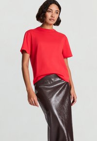 T-shirt rossa in cotone con scollo rotondo e maniche corte, abbinata a una gonna marrone lucida in pelle con un design lineare.