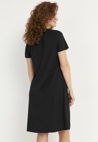 Lyhythihainen musta mekko, joka on valmistettu sileästä kankaasta, sisältää yksinkertaisen muotoilun ja rentoa istuvuutta, ja se ulottuu juuri polvien ylle.