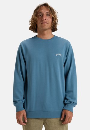 Blauwe katoenen sweatshirt met lange mouwen, ribbelmanchetten en een ronde hals. Voorzien van een klein wit logo op de linkerkant van de borst.