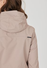 Lys beige hættejakke med en tekstureret stof, synlige stikninger og en sort accentstribe på ryggen.