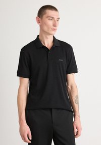 Melns polo krekls ar īsām piedurknēm un apkakli, ar diskrētu "BOSS" logotipu uz krūtīm. Gluda tekstūra, piegriezts fit.
