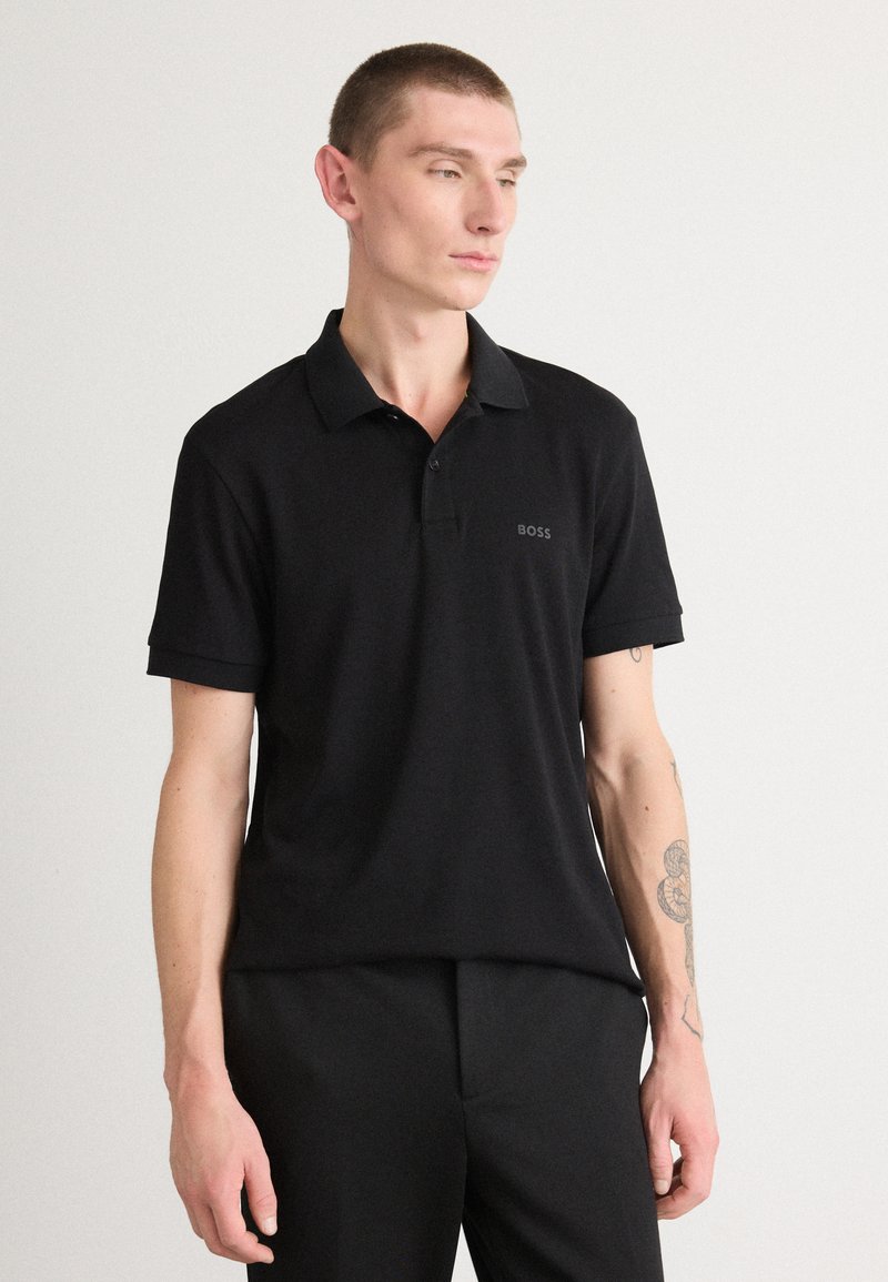 Melns polo krekls ar īsām piedurknēm un apkakli, ar diskrētu "BOSS" logotipu uz krūtīm. Gluda tekstūra, piegriezts fit.