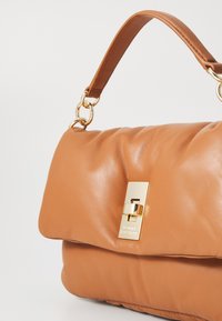 Borsa a mano in pelle color nocciola con forma strutturata, caratterizzata da un dettaglio in oro e una finitura liscia. La tracolla è realizzata in pelle marrone chiaro.