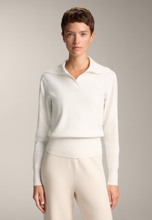 Pullover bianco in maglia con ampio colletto e orlo a costine. Maniche lunghe, tessuto testurizzato e silhouette aderente. Abbinato a pantaloni beige.