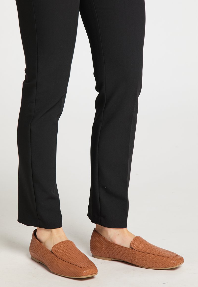 Brune vævede loafers med flad sål og firkantet tådesign. Båret sammen med sorte tætsiddende bukser, der fremhæver en slank silhuet.