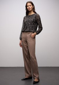 Bluzka z długim rękawem w ciemnoszarym kolorze z geometrycznym wzorem, zestawiona z jasnobrązowymi, dopasowanymi spodniami oraz czarnymi balerinami na szpic.