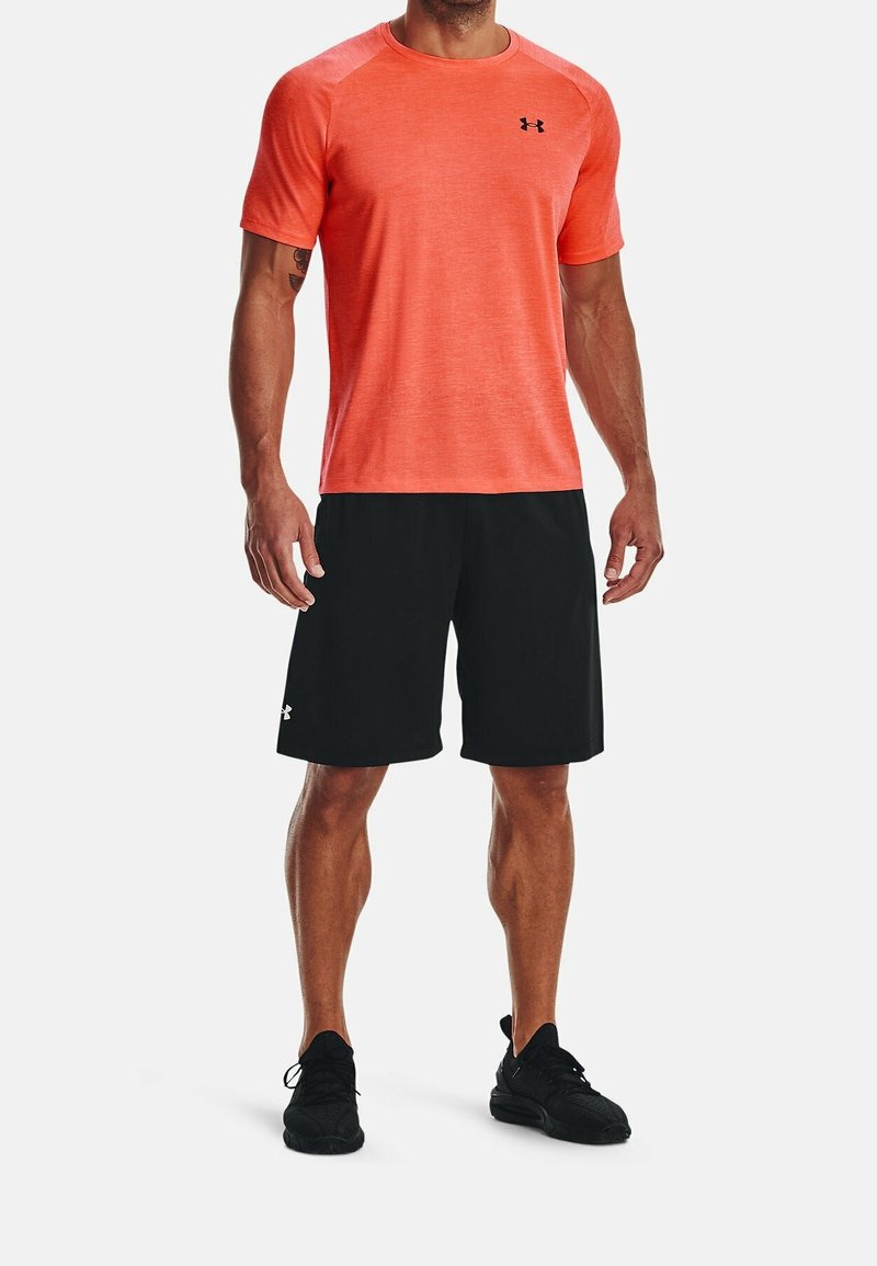 Conjunto deportivo para hombre que incluye una camiseta de manga corta naranja y pantalones cortos negros, fabricado con material transpirable y con un corte relajado.