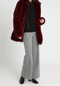 Burgundowy płaszcz z sztucznego futra o miękkiej fakturze, zestawiony z czarnym swetrem w splot kablowy i szarymi spodniami w ząbkowaną kratę o szerokich nogawkach. Czerną błyszczącą parą botków za kostkę.