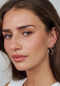 Örhängen av guld och silver i form av abstrakta tårar, med en slät yta och minimalistisk design.