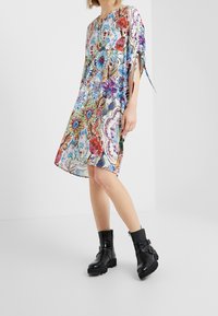 Mehrfarbiges Blumenkleid mit lockerer Passform, kurzen Ärmeln und seitlichen Schlitzen, kombiniert mit schwarzen Knöchelstiefeln mit Schnallen und klobigen Sohlen.